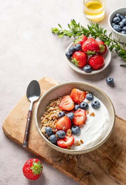 Ballı, dutlu ve kaşıklı bir arka planda, tahtadan yapılmış bir kasede, yaban mersinli ve çilekli doğal Yunan yoğurdu. Sağlıklı ve besleyici kahvaltı konsepti. Üst görünüm, alanı kopyala.
