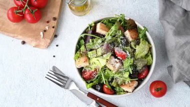 Marul, domates, kızarmış ekmek, zeytin ve parmesan peynirli vejetaryen salatası hafif bir arka planda taze sebze, yağ ve çatal bıçakla birlikte. Sağlıklı beslenme konsepti. Üst görünüm.