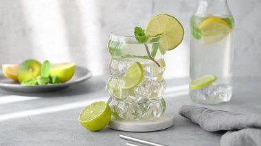 Taze kireç, nane ve buzlu mojito kokteyli. Arka planda hafif bir şişe ve hareketli bir gölge var. Turunçgil ile ferahlatıcı bir yaz içeceği kavramı. Ön görünüm.