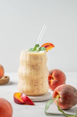 Şeftalili ve muzlu meyve püresi mermer tezgahın üzerinde tropikal meyveler ve güneş ışığıyla aydınlık bir zeminde. Reklam menüsü ya da afiş kafe için sağlıklı beslenme ve detoks diyeti kavramı. Ön görünüm, boşluğu kopyala.