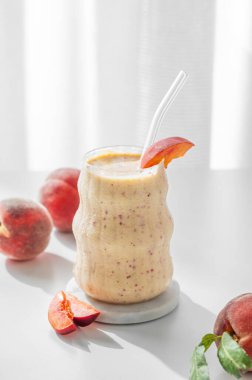 Şeftalili ve muzlu meyve püresi, cam kenarındaki beyaz bir masada, tropik meyve dilimleri ve sabah güneşiyle birlikte. Sağlıklı beslenme ve pankart kafenin reklam merusu için detoks diyeti kavramı. Ön görünüm, boşluğu kopyala.