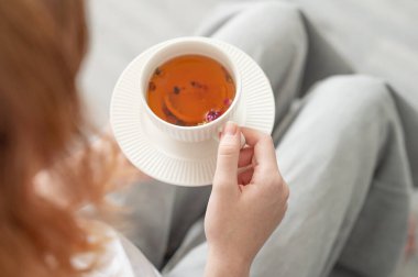 Sıcak, aydınlık bir odada elinde limonlu ve otlu çay tutan bir kadın. Kahvaltı ve sağlıklı beslenme konsepti. Üst görünüm ve kopyalama alanı.