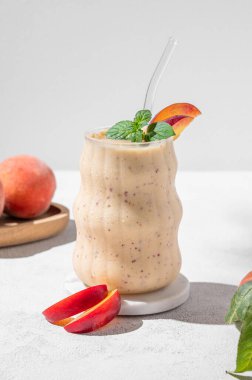 Şeftalili ve muzlu meyve püresi mermer tezgahın üzerinde, tropikal meyveli, güneş ışığı olan bir cam üzerinde. Reklam menüsü ya da afiş kafe için sağlıklı beslenme ve detoks diyeti kavramı. Ön görünüm, boşluğu kopyala.