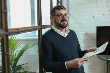 Happy Caucasian man holding documents and standing in the office, copy space