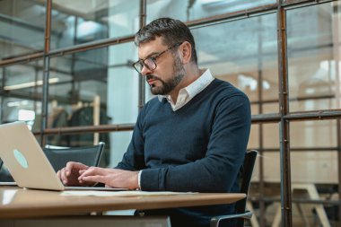 Male economist sitting in chair while preparing report on modern loft workstation interior