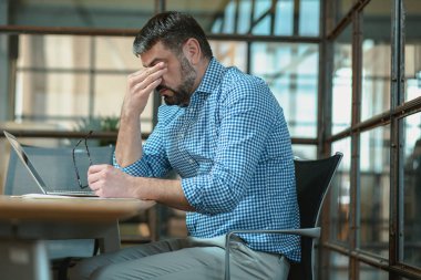 Stressed man suffering from headache while working with laptop in the office