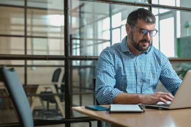 Yeni projede çalışırken ofis masasında dizüstü bilgisayar kullanan beyaz bir adam.