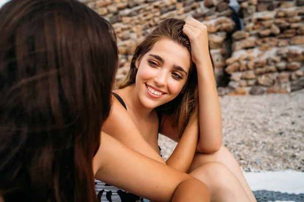 Positive Giovani Amiche Costume Bagno Seduti Sulla Spiaggia Ghiaia Parlando — Foto Stock