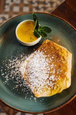 Lezzetli ev yapımı, şeker tozu ve kremalı kremalı krep ve ahşap yemek masasının üzerine yerleştirilmiş nane yapraklarının yakın görüntüsü.