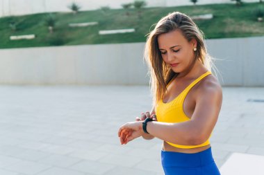 Genç sporcu kadın, şehir dışında spor yapmadan önce akıllı saatleri kontrol ediyor.
