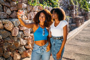 İki genç kadın gülümseyip günün tadını çıkarırken selfie çekiyorlar.