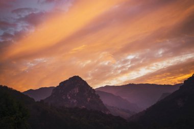 Şok edici altın gün batımında, sakin dağ manzarası doğanın güzelliğini ve sükunetini sergiliyor.