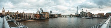 Panoramic cityscape of london showcasing iconic landmarks along the river thames, including the shard and millennium bridge, under a cloudy sky clipart