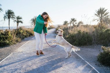 Bir kadın, güzel manzaralı sahil yolunda neşeli ve keyifli bir şekilde köpeğiyle yürüyor.