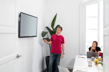 Modern ofiste sunum sırasında uzaktan kumanda ve TV ekranı kullanan pazarlama uzmanı