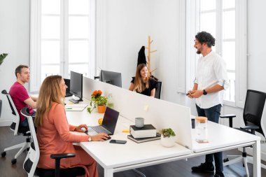 Parlak modern ofiste bir proje üzerinde çalışan iş arkadaşları, fikirleri ve stratejileri tartışıyor.