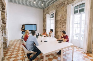 Pazarlama ekibi toplantı odasında televizyon ekranı ile stratejiyi tartışıyor.