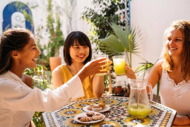 Çok ırklı değişim öğrencileri sağlıklı meyve suyuyla kadeh kaldırarak egzotik bir bahçe bahçesinde eğleniyorlar.