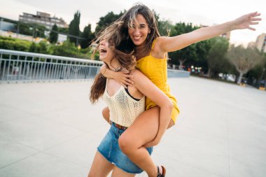 İki neşeli bayan arkadaş sırtımda gezintiyle eğleniyor, gülüyor ve şehir ortamında eğleniyorlar.