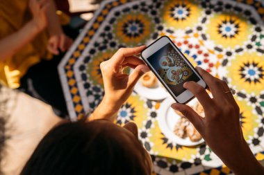 Değişim öğrencisi geleneksel Fas yemeklerini seramik masa üzerinde akıllı telefon kullanarak çekiyor.