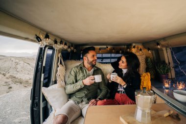 Genç çift rahat karavanlarında rahatlayıp kahve içiyorlar. Göçebe yaşam tarzının ve minibüs yaşamının özgürlüğünün tadını çıkarıyorlar.