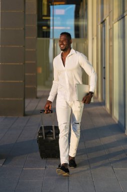 Genç siyahi girişimci havaalanına geliyor bavulunu çekiyor ve laptop, iş seyahati konseptini taşıyor.