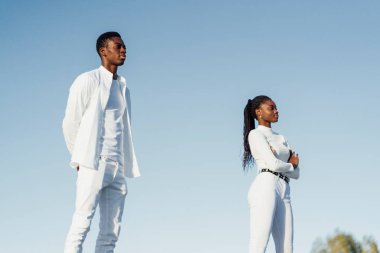 Mavi gökyüzüne karşı duran mankenler minimalist beyaz giysiler sergiliyor.