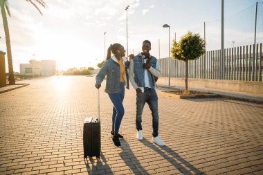Genç siyah turistler, gün batımında havaalanının dışında birlikte yürürler.
