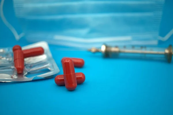 Medical, Covid-19 and healthcare background with red capsules scattered on blue alongside an empty blister pack with syringe and face mask