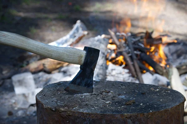 Camp fire in a forest with chopper lodged in a log of wood in the foreground in a healthy active lifestyle concept
