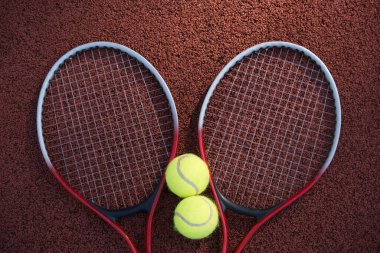 Sert tenis kortu yüzeyinde iki sarı tenis topu ve iki raket, üst manzara tenis sahnesi.