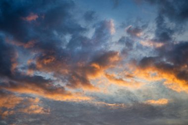 Gökyüzü alacakaranlıkta parlak mavi ve turuncu renklerin birleşimiyle kümülüs bulutları gökyüzünü kaplıyor ve dramatik bir etki yaratıyor.