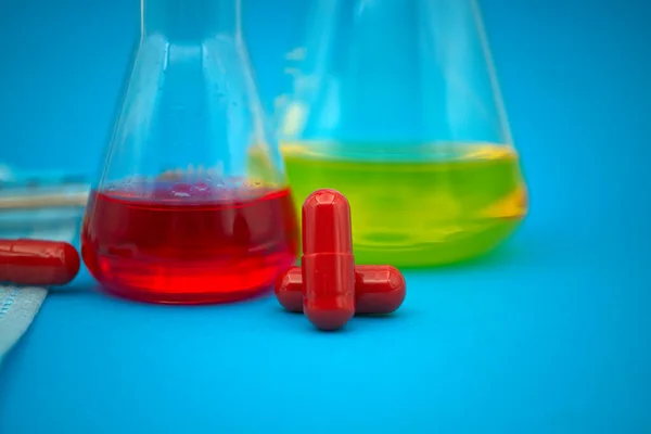 stock image Medical, healthcare or Covid-19 still life with red capsules and chemical solution in a flask over a blue background