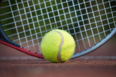 Beyaz çizginin yanında tenis raketi ve sarı tenis topu alçak açılı tenis sahası sahnesi.