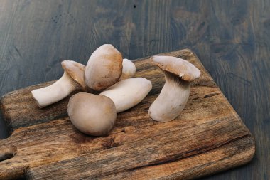 Taze istiridye mantarları, çeşitli boyutlarda, ahşap kesim tahtasının üzerinde dinlenme, arka plan gri tonlu ahşap yüzey, canlı yemek hazırlama sahnesi