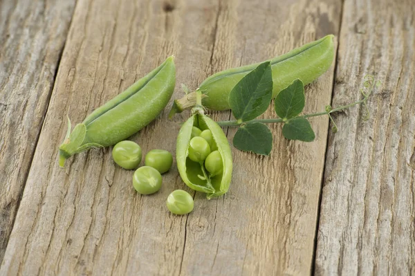 Group of fresh green peas, pea pods with green leaves and open pea pod on a wooden surface