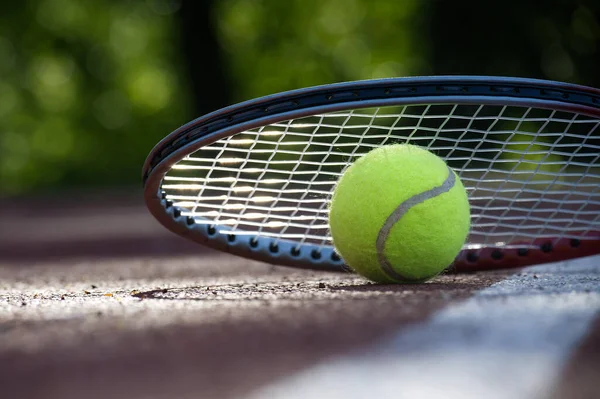 Beyaz çizginin yanında tenis raketi ve sarı tenis topu alçak açılı tenis sahası sahnesi.