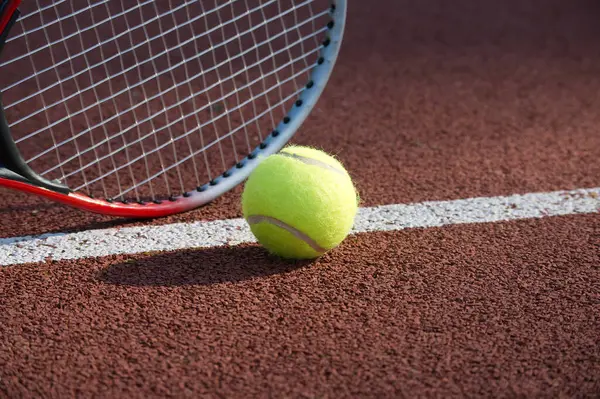 Tennis racquet and yellow tennis ball near white line, outdoor court tennis scene in low angle view