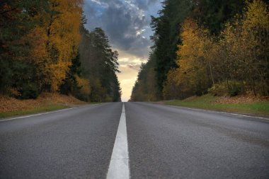 Mesafe boyunca uzanan boş, asfalt bir yolun hakim olduğu sakin bir sabah sahnesi.