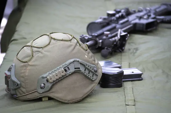 stock image Military helmet alongside rifle with a scope on a cloth surface, also magazines visible in the setup, contributing to the military theme of the equipment displayed