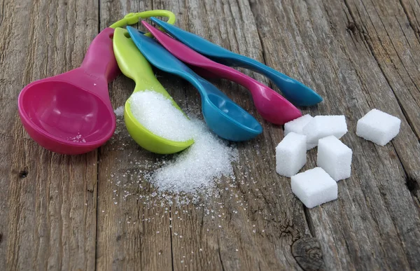 Set of colorful plastic measuring spoons, in green, pink, blue, purple, and yellow, with sugar spilled around on a rustic wooden surface, measuring utensils in a kitchen setting