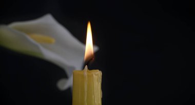 Beyaz zambakların yanında yanan sarı mum, koyu arkaplanla çelişiyor, mum yumuşak alevi huzurlu ortamı zenginleştiriyor.