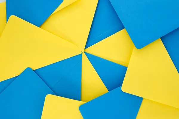 Blue and yellow paper envelopes organized in a symmetrical pattern gives the appearance of a three-dimensional, exploding geometry that adds a sense of depth and vibrancy