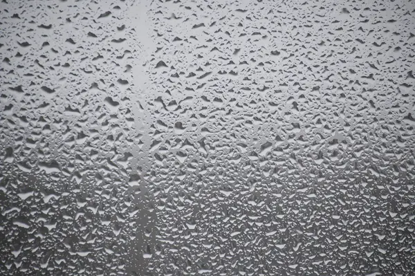 Raindrops on a window, precipitating from a drizzle outside, create a serene ambiance associated with the rainy season