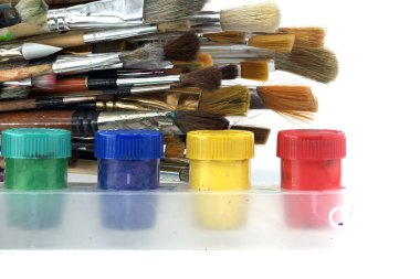 Array of paintbrushes of different sizes and colors alongside cans of acrylic paint with visible colors including red, yellow, blue, and green arranged on a white surface clipart