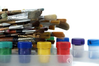 Array of paintbrushes of different sizes and colors alongside cans of acrylic paint with visible colors arranged on a white surface clipart