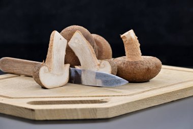 Kesme tahtasındaki taze şitake mantarları, beyaz iç organlarını, besleyici ve tıbbi yapısını ortaya çıkarmak için bir mantarı dilimlenmiş halde, Lentinula edodes