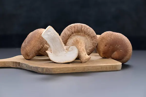 stock image Fresh shiitake mushrooms on a cutting board, with one mushroom sliced open to reveal its white interior, nutritional and medicinal, Lentinula edodes