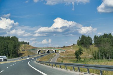 Üstgeçit köprüsü olan güzel manzaralı otoyol, araçlar sürüyor, ve güneşli bir günde bulutlu açık mavi gökyüzü..