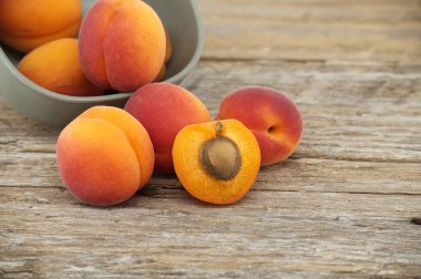 Collection of ripe whole apricots and one cut in half to reveal its interior, rustic wooden table clipart